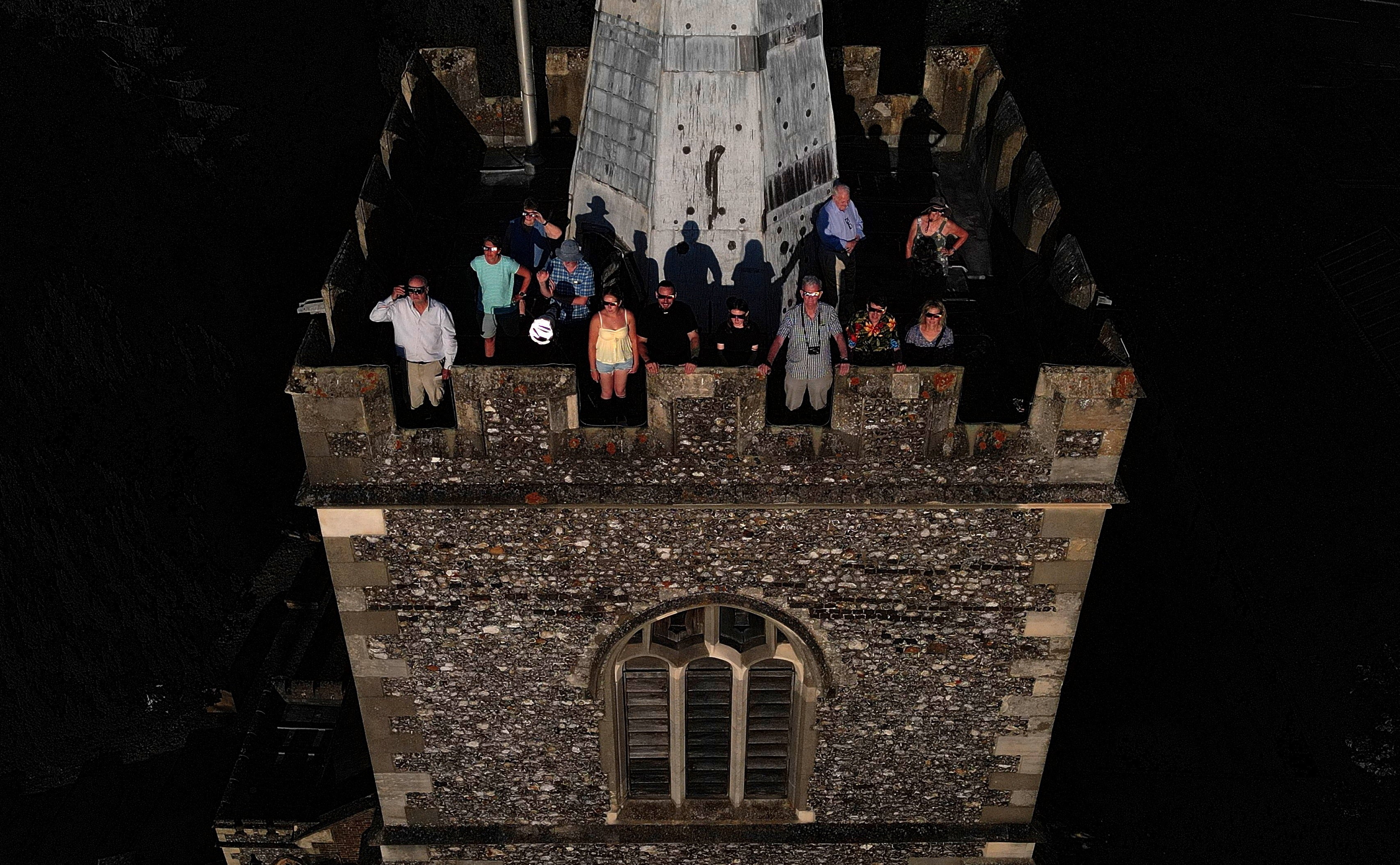 People wear special protective glasses to observe a partial solar eclipse at the top of a church bell tower.