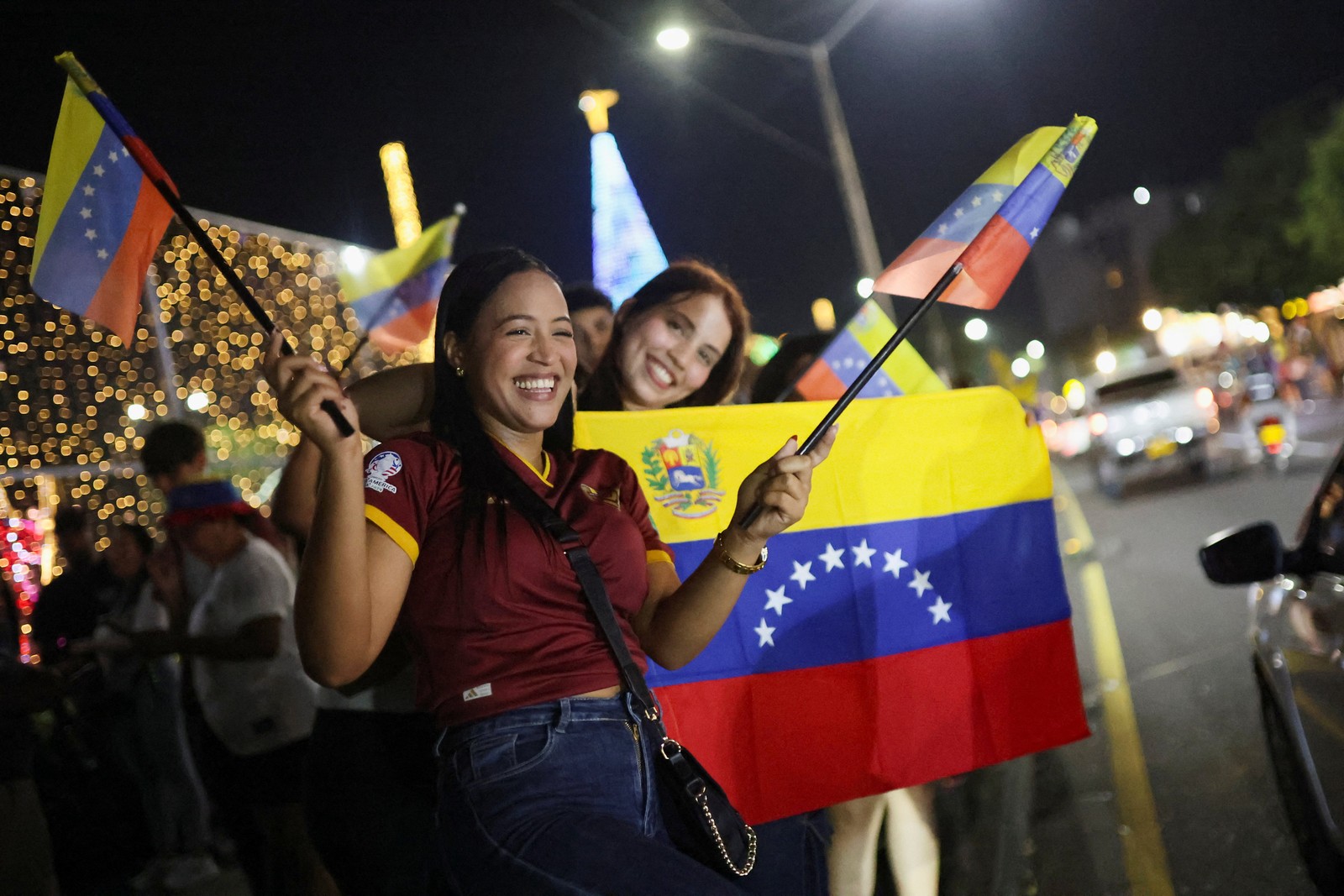 Several people smile and wave Venezuelan flags beside a road.