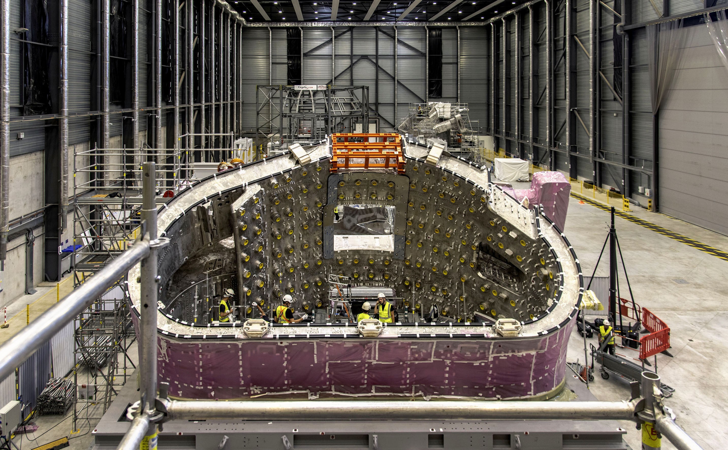 A large and complex metal segment of a fusion reactor lies on its side in a tall building