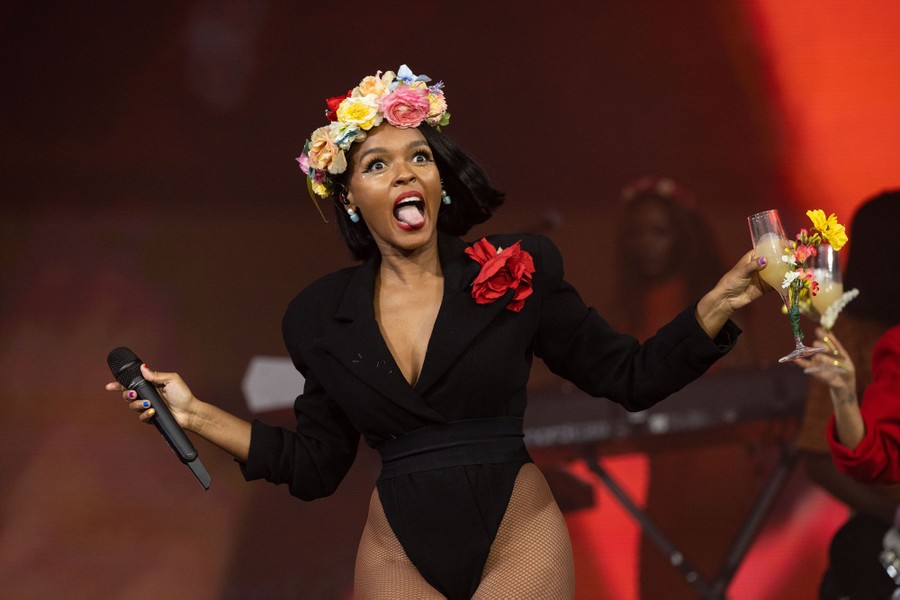 A performer makes a face while onstage, holding a microphone and a long-stemmed drinking glass.