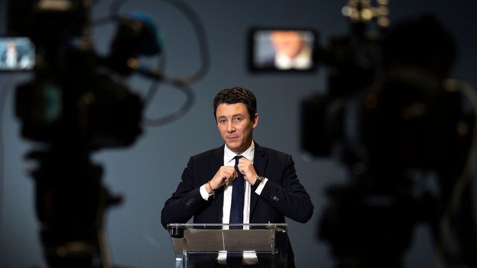 Benjamin Griveaux stands in front of video cameras while tightening his tie.