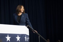 Kamala Harris smiles and walks up steps at a campaign event.