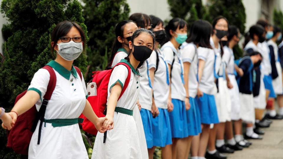 Secondary-school students wearing face masks hold hands, forming a long human chain.