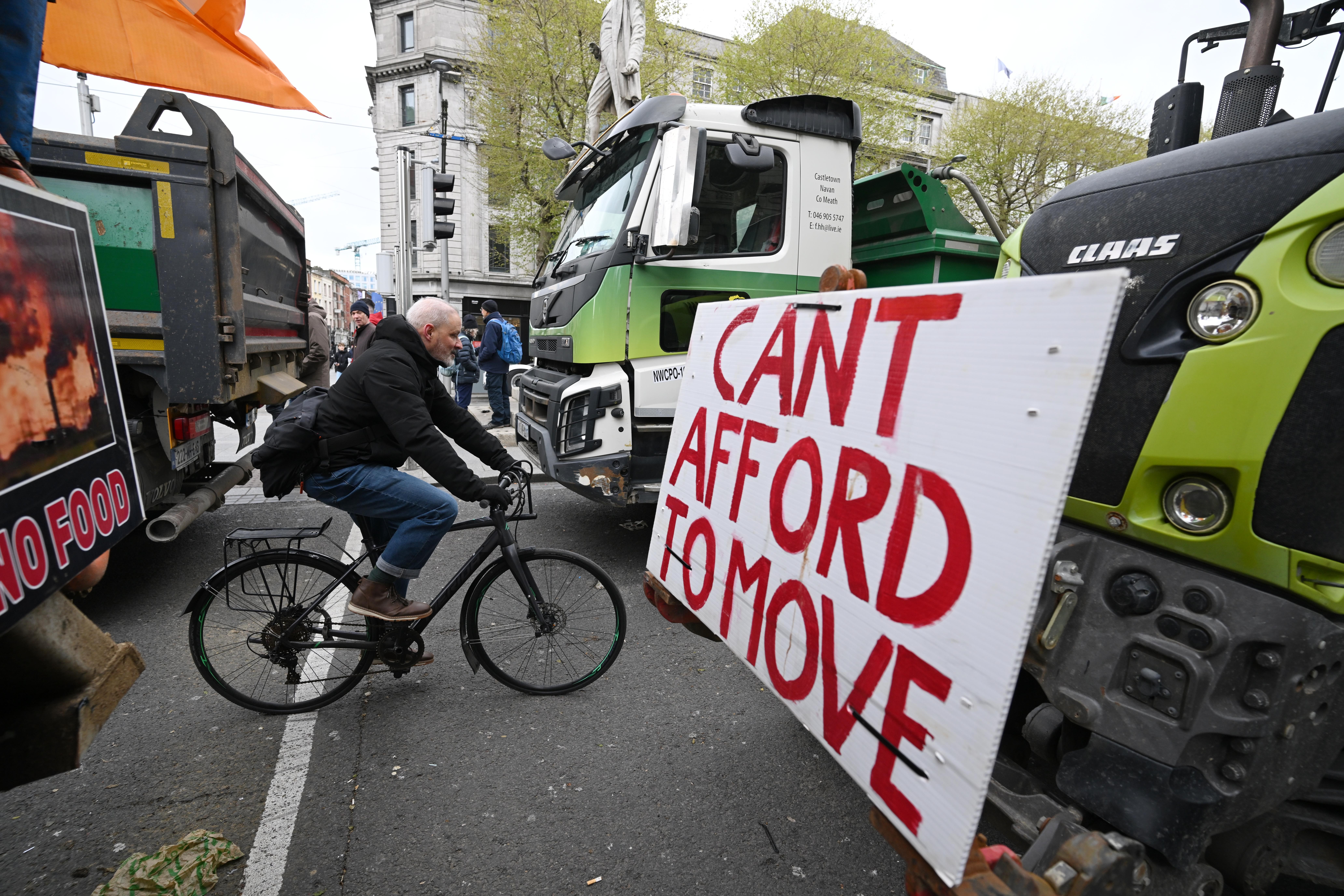 A person rides a bike through trucks and tractors parked in a street during a protest.
