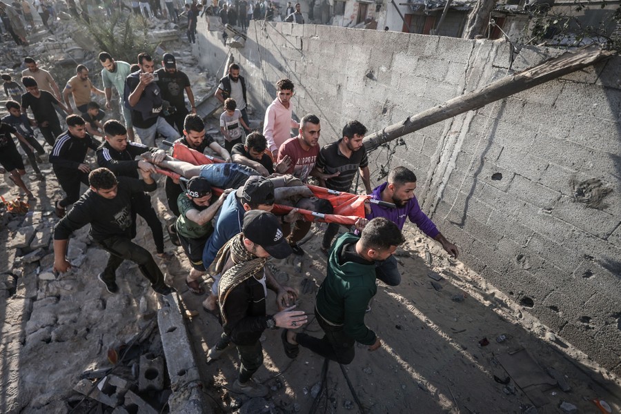 A crowd carries a person on a stretcher away from a destroyed building.
