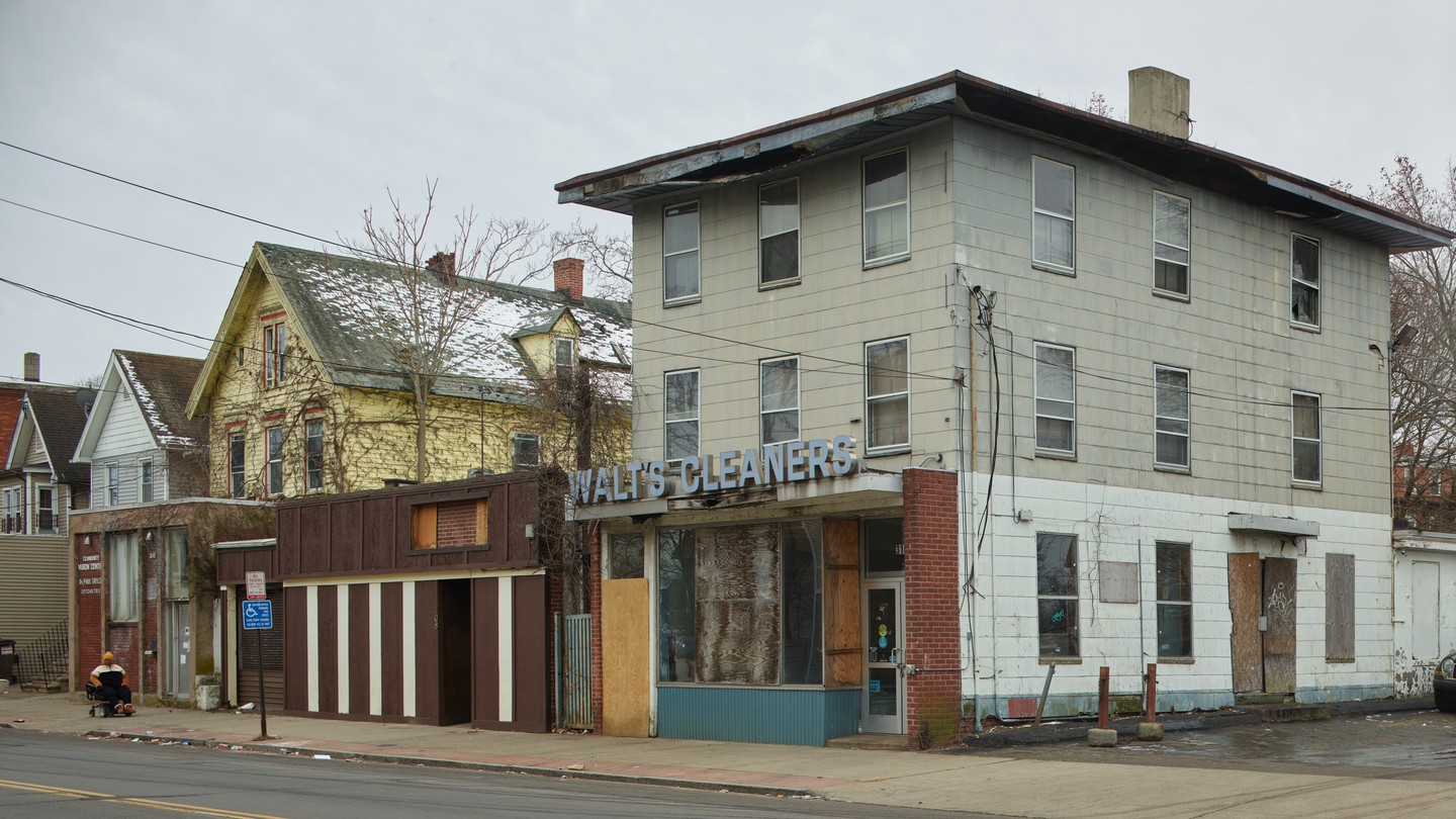 Photo of a slightly run-down laundromat on a street with boarded-up building