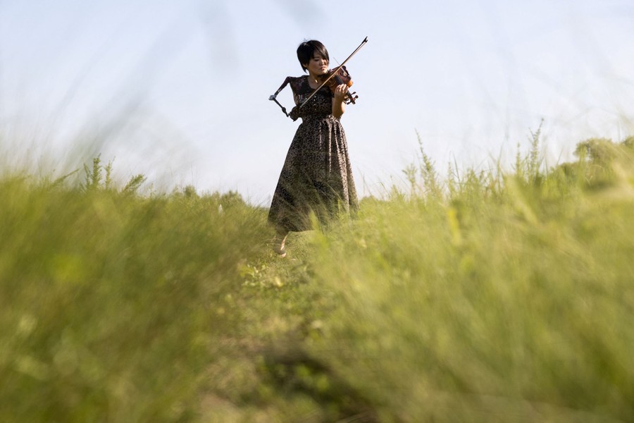 A musician plays the violin while standing in a field, using her prosthetic arm.