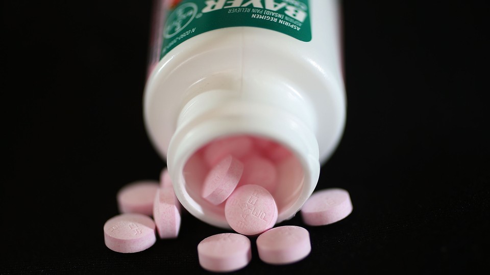 A bottle of Bayer aspirin spills pink pills labeled "Bayer"