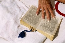 An older person's hand holds a book open on a towel.