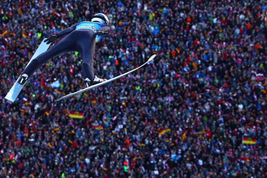 A ski jumper in mid-air, with a large crowd of onlookers in the background