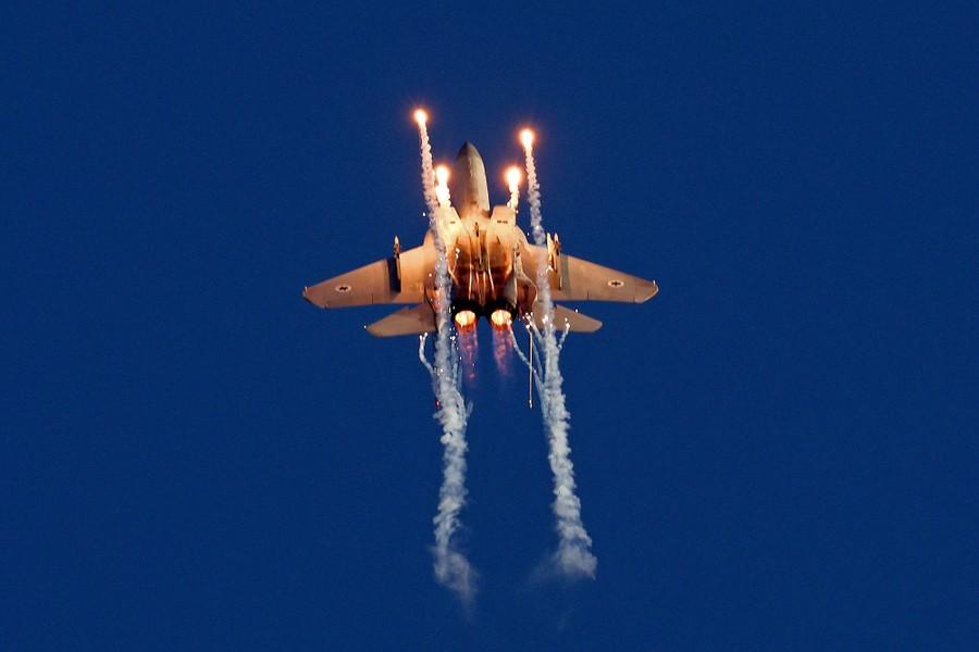A fighter jet launches flares as it flies overhead.