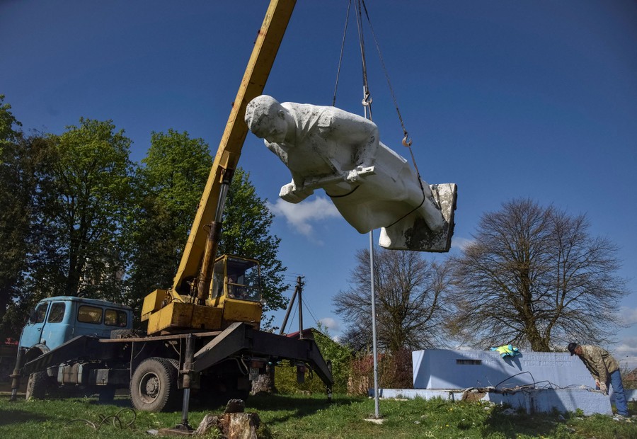 A statue is lowered from a podium, hanging from a crane.