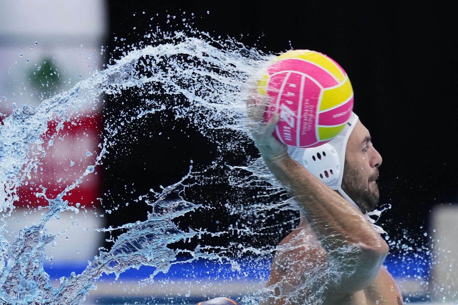 A water polo player throws a ball, splashing pool water all over the place.