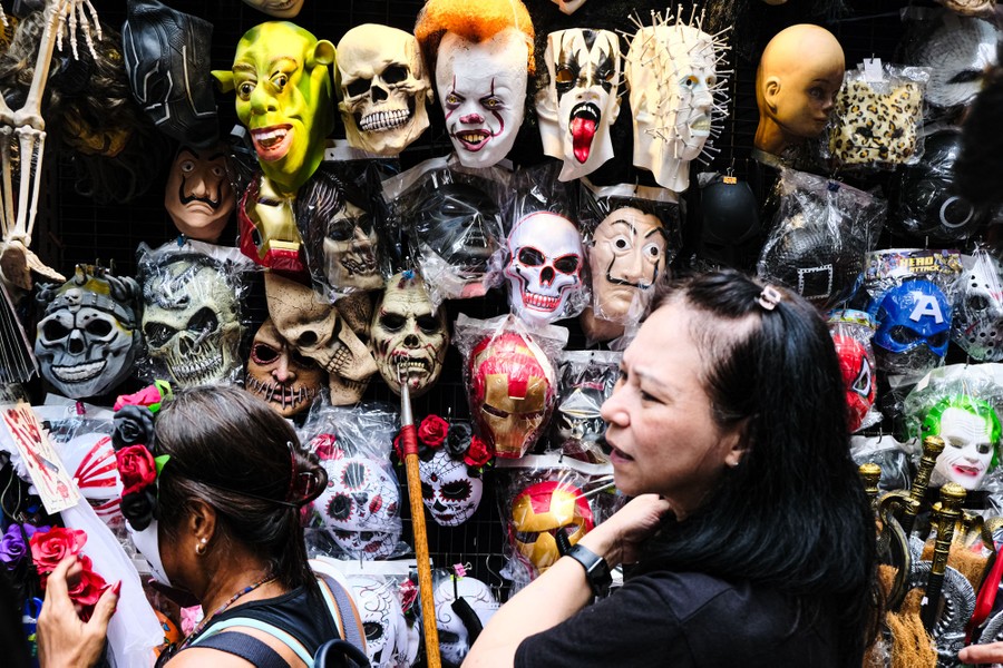 People shop at a store that displays dozens of rubber Halloween masks.