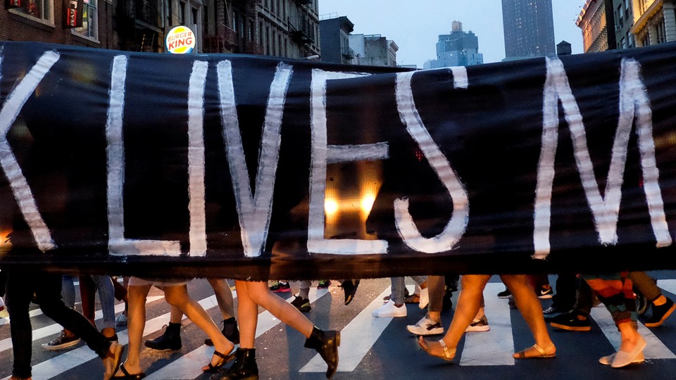 People walking across a crosswalk behind a Black Lives Matter banner