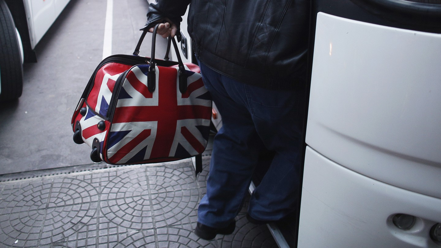 A man carries a bag with the British flag onto a bus.