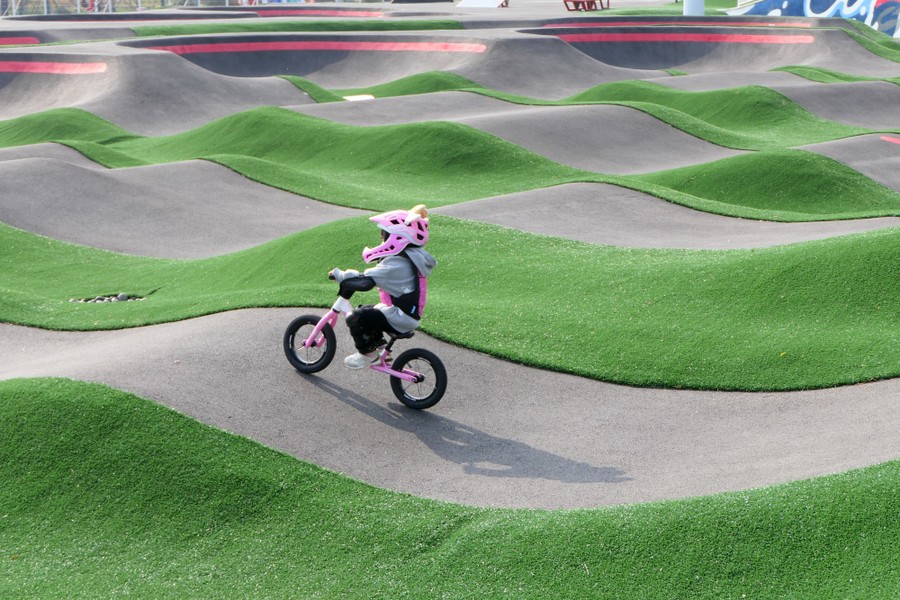 A child rides a bicycle on an undulating track in a park.