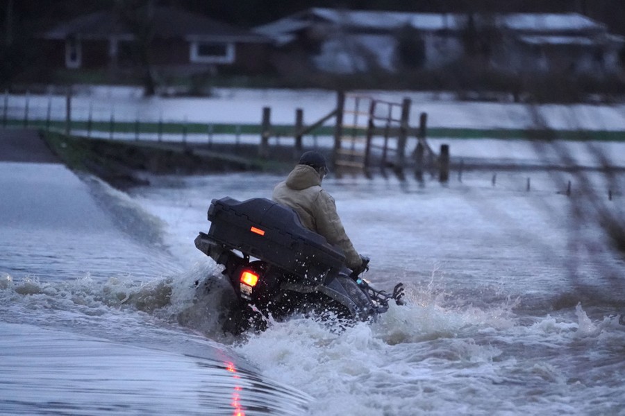 A man holds on to the handlebars of his all-terrain vehicle as he is swept off a road by flowing floodwater.