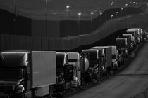 Black-and-white photo of a line of trucks near the Mexico-U.S. border