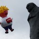 A giant inflatable blimp caricaturing Boris Johnson hovers beside a statue of Winston Churchill.