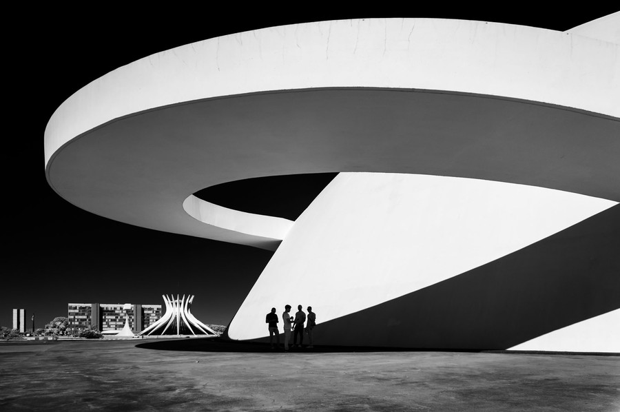 A group of four people stand beside a large, swooping modern building.