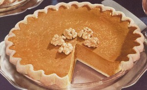 A closeup of a pumpkin pie with walnuts and a slice missing