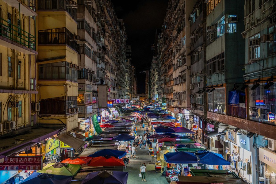 People walk at an outdoor market between tall buildings at night.