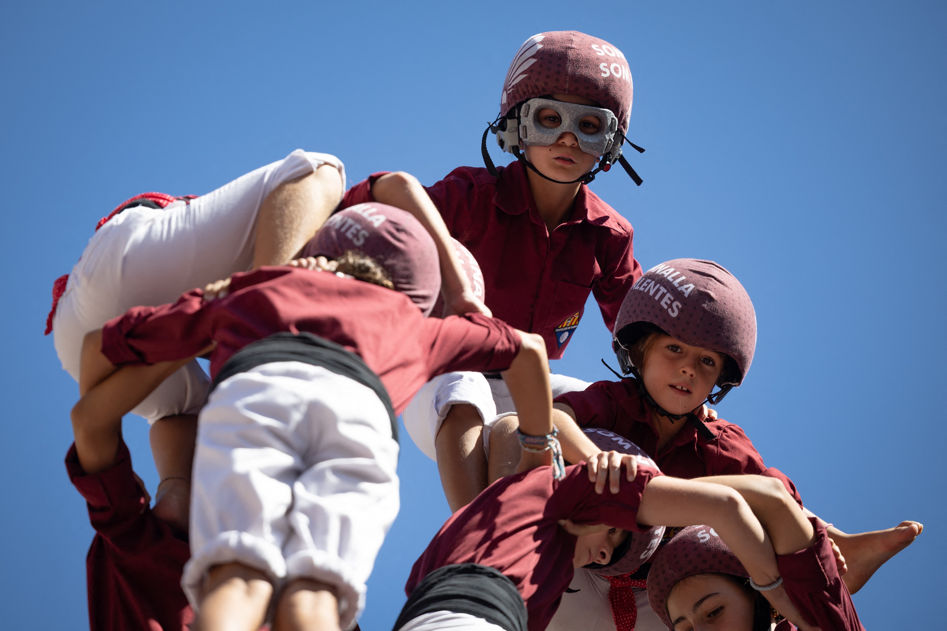 Children at the top of a human tower wear safety helmets and goggles.