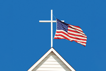 photo-illustration of white cross atop white wooden church steeple with U.S. flag flying from it against blue sky