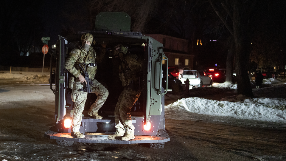 Masked and armed federal immigration officers in a vehicle at night with snow and ice on the street