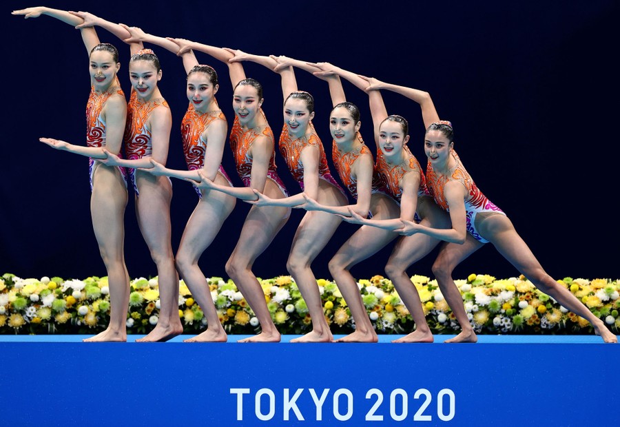 A team of swimmers poses with arms joined to form two lines, beside a pool.