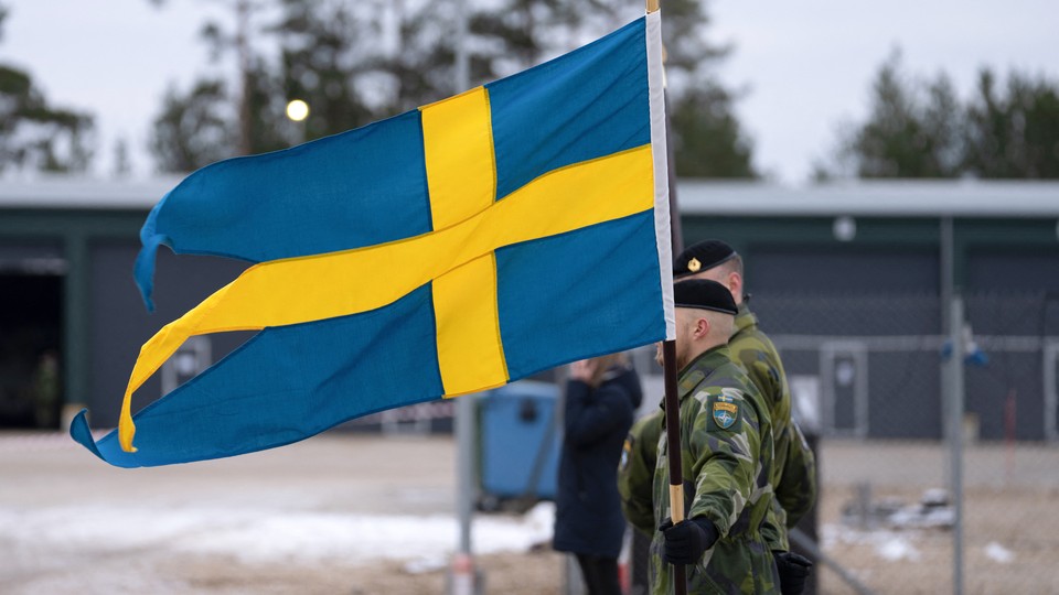 Soldiers stand next to a Swedish flag.