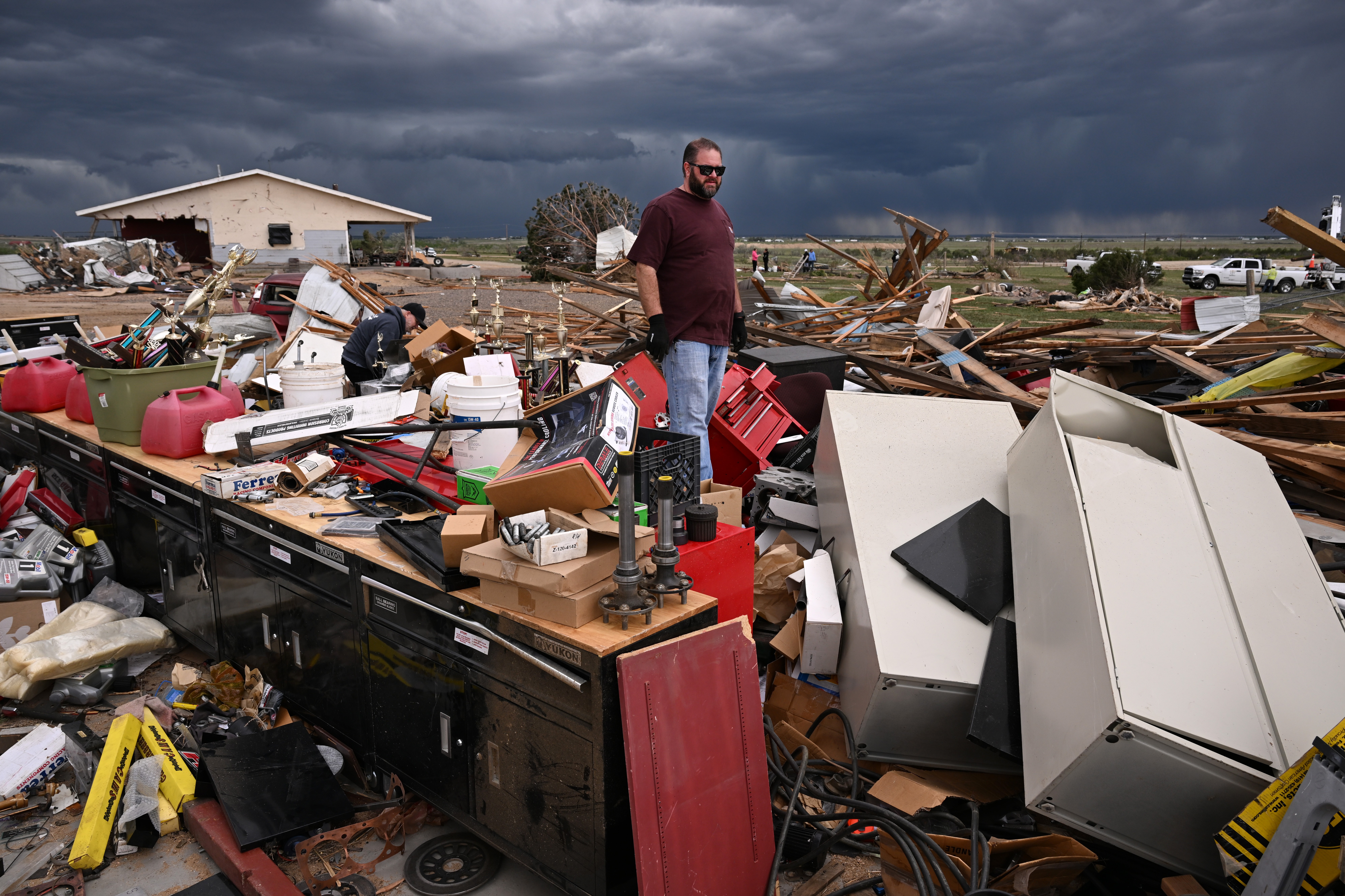 A man stands in the middle of a broad field of debris left after a tornado destroyed a house.