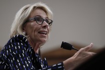 Betsy DeVos gestures while sitting at a microphone