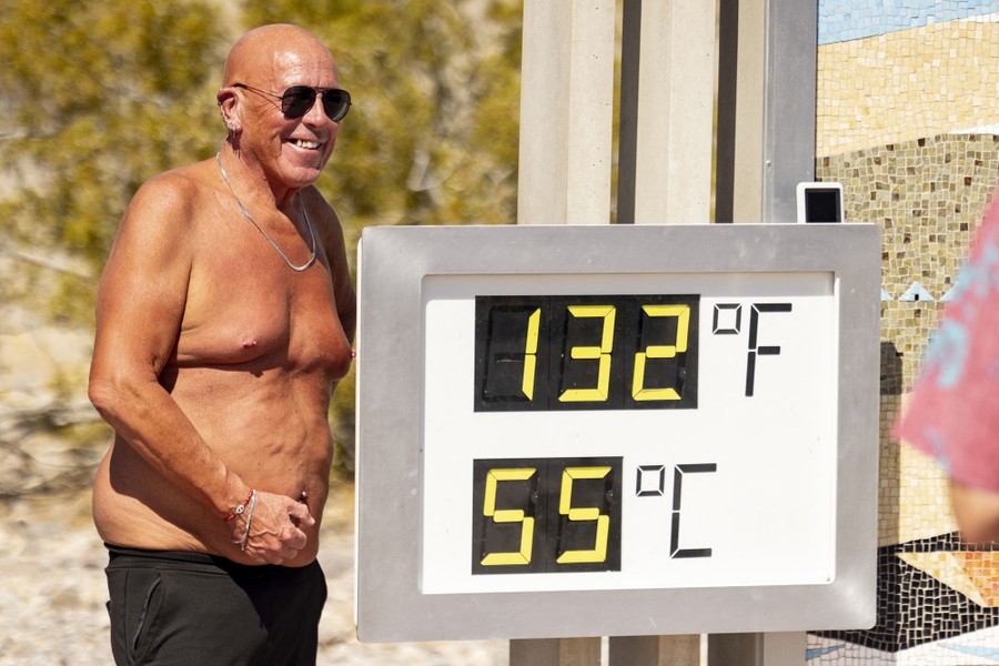 A shirtless visitor poses in front of a sign reading 132 degrees Fahrenheit and 55 degrees Celsius.