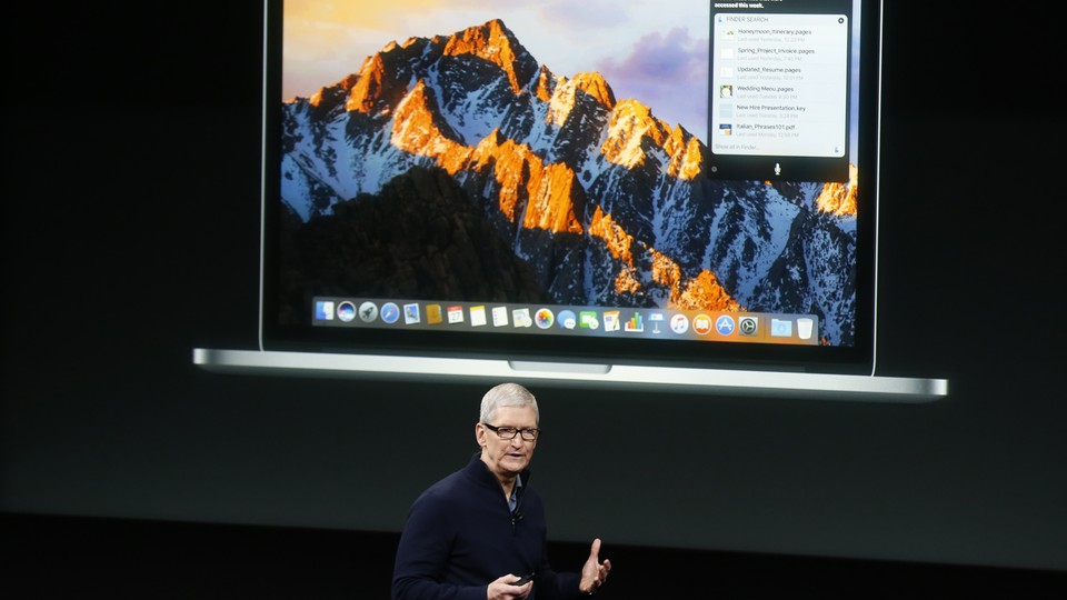 Tim Cook stands in front of a projected image of an Apple laptop.