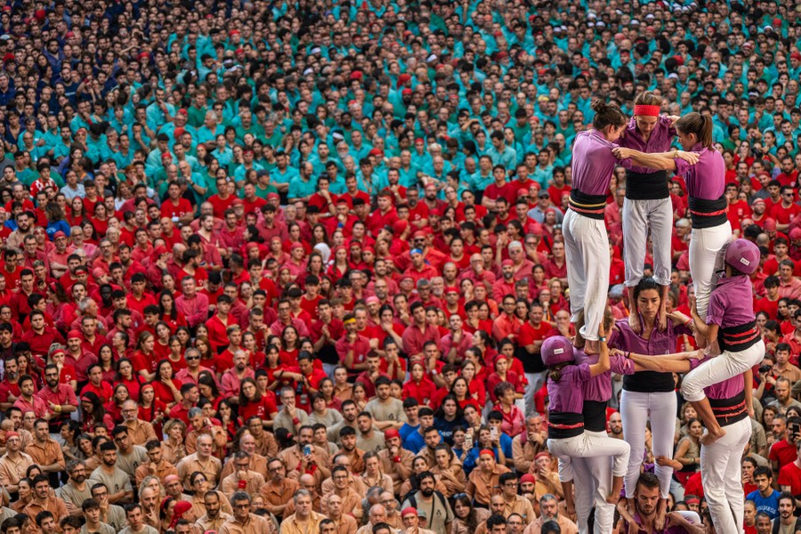 A large crowd of competitors and onlookers watch as a group of people climb onto each other's shoulders to form a tower.