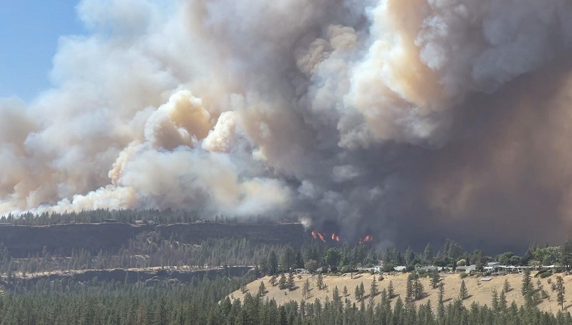 Large smoke plumes rise from a wildfire seen on a distant bluff.