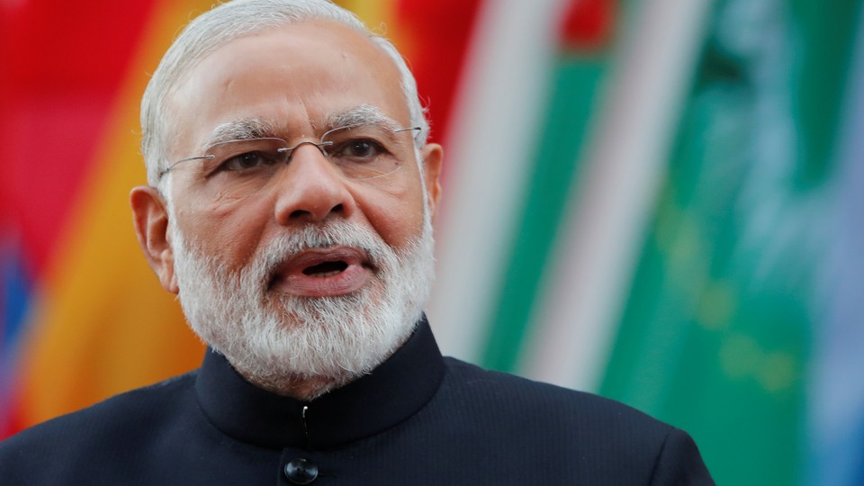 India's Prime Minister Narendra Modi looking at the camera in front of a row of flags.