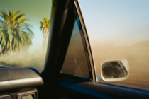 photo looking out of car window with rear-view mirror and palm trees