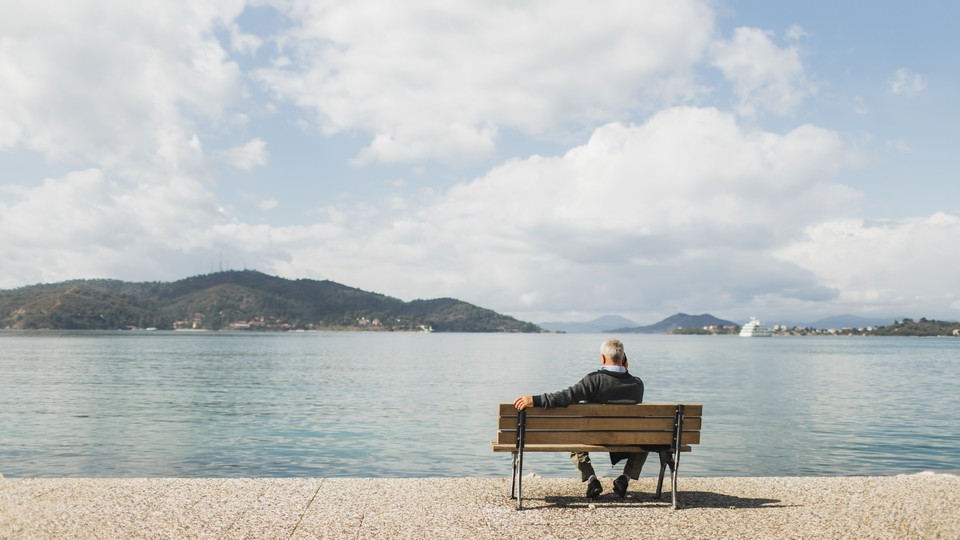 An older man sitting on a bench looking out at the water