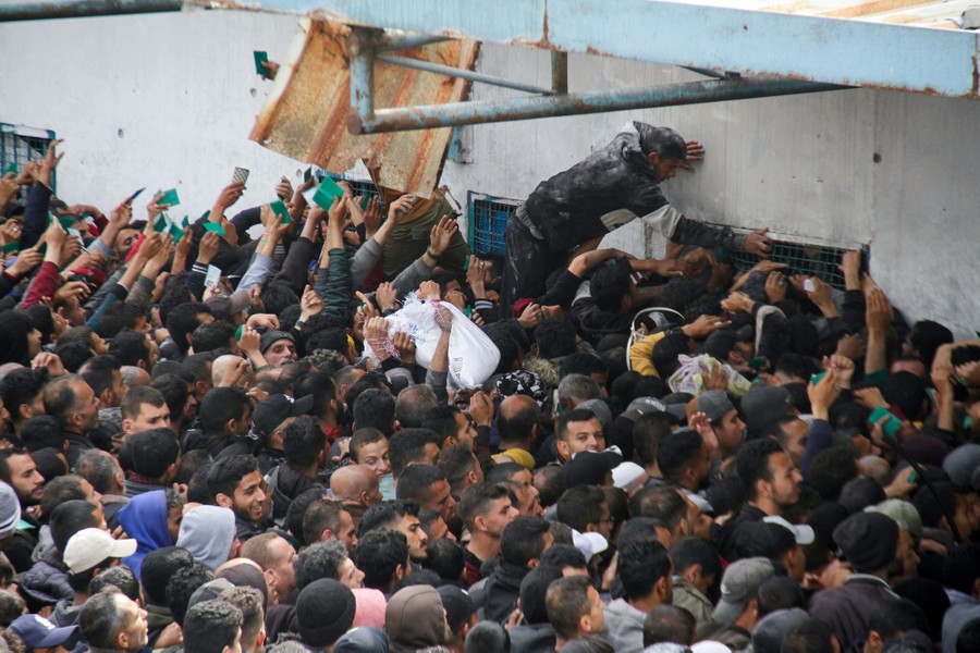 A crowd of people press close to a building, many of them reaching out their hands.