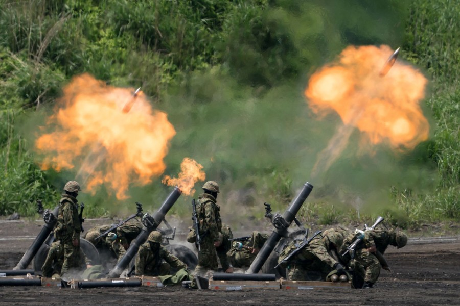 Soldiers stand beside several mortars that are firing, launching shells.