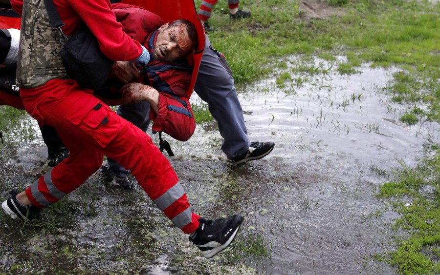 Several emergency responders carry an injured man across a puddle.