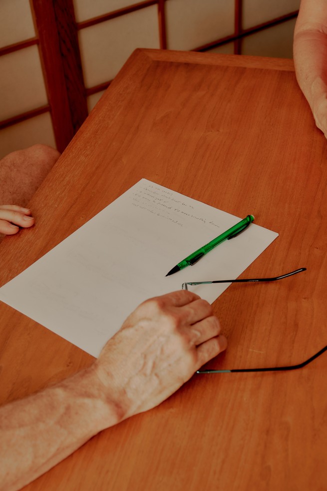 A hand holds glasses on a table next to a piece of paper