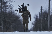 A soldier carries a drone on their shoulder while walking on a snow-covered road.