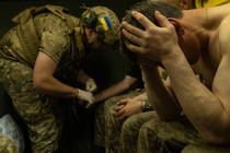 A Ukranian soldier holds his head in his hands while another one behind him treats another soldier.