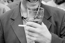 A man smiling with a pint and cigarette in hand.