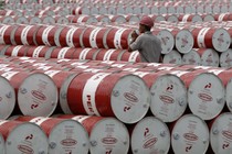 A worker walks between stacks of red and white oil barrels.