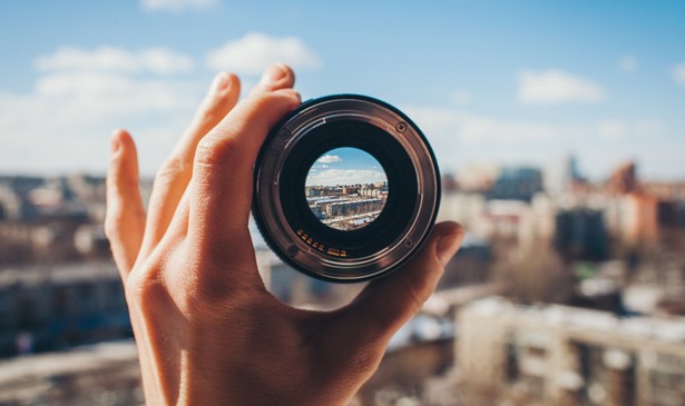 A view of a city through a camera lens held up by a hand